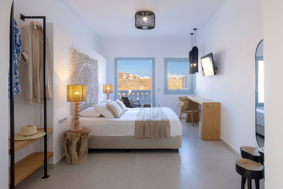 A modern bedroom with a bed, bedside tables, a desk, and a view of the outdoors.