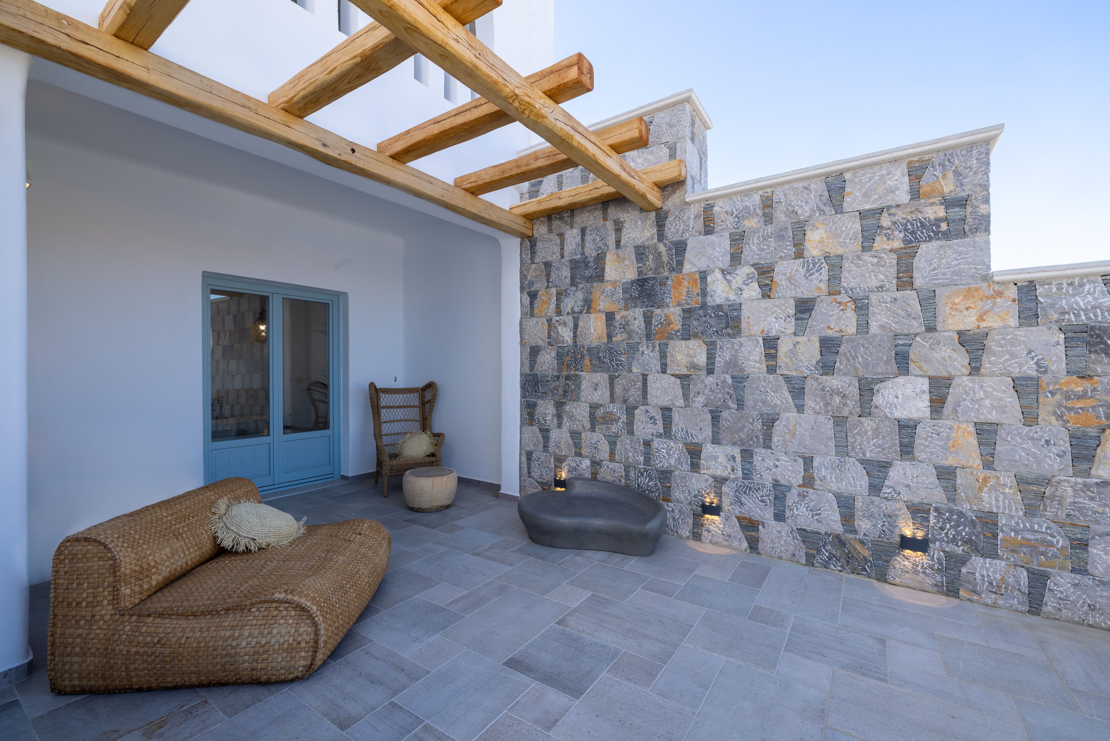 Un área de estar al aire libre con pared de piedra, vigas de madera y una puerta azul.