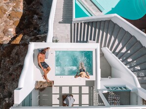 A rooftop pool area with a hot tub, a person relaxing on a towel, and another person cleaning the pool. - Infinity Blue Suites (Astypalaia)