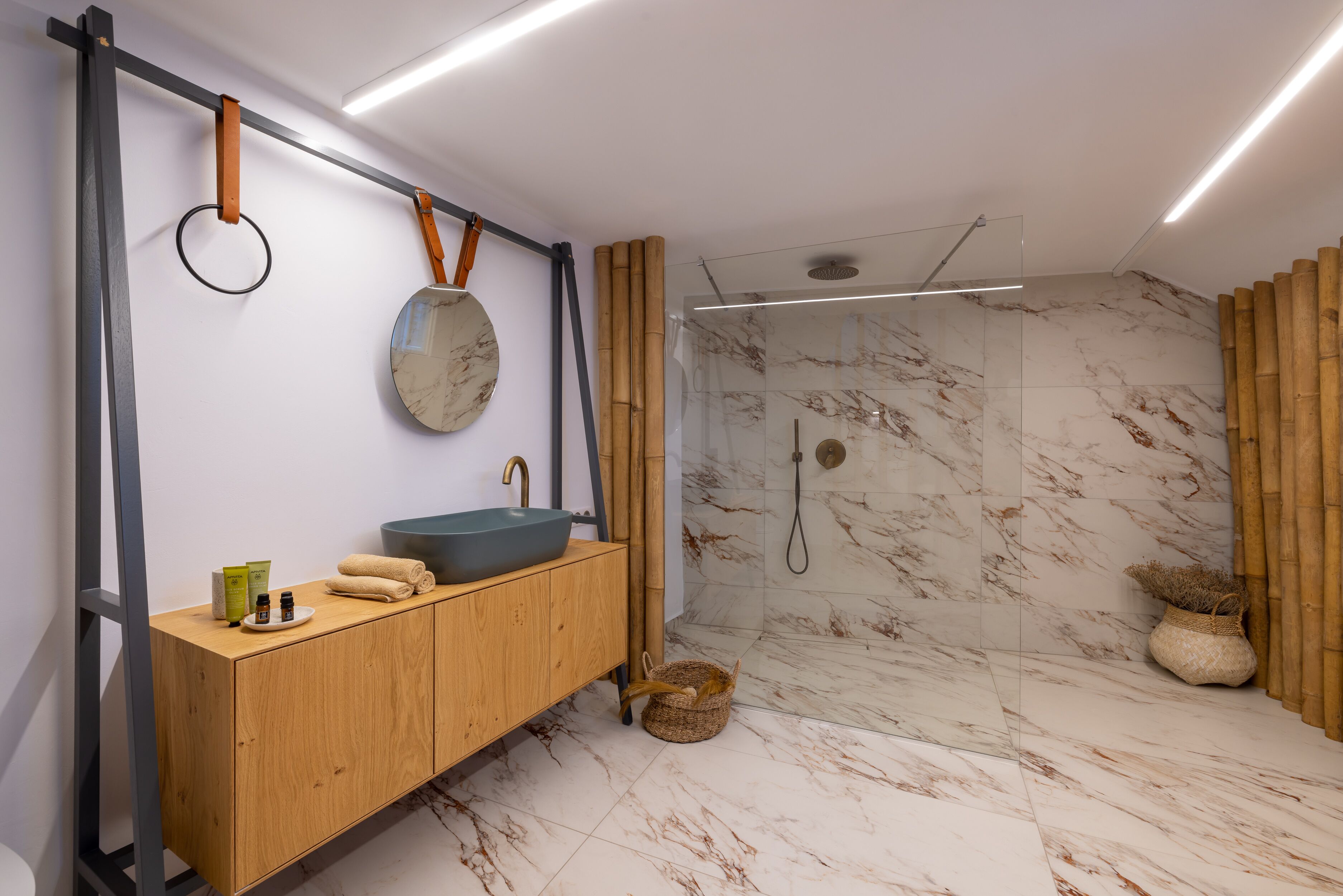 A modern bathroom with a wooden vanity, a round mirror, and a glass-enclosed shower.