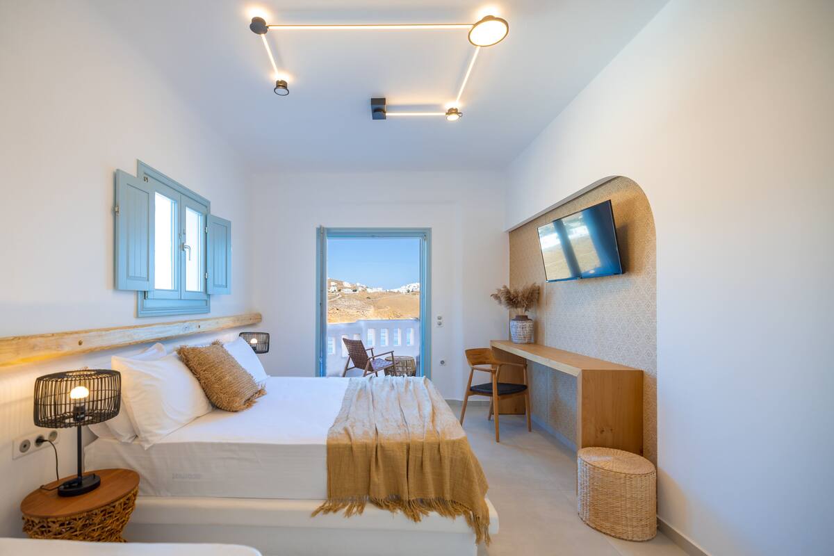 A modern bedroom with a bed, bedside table, lamp, and a view of the outdoors.