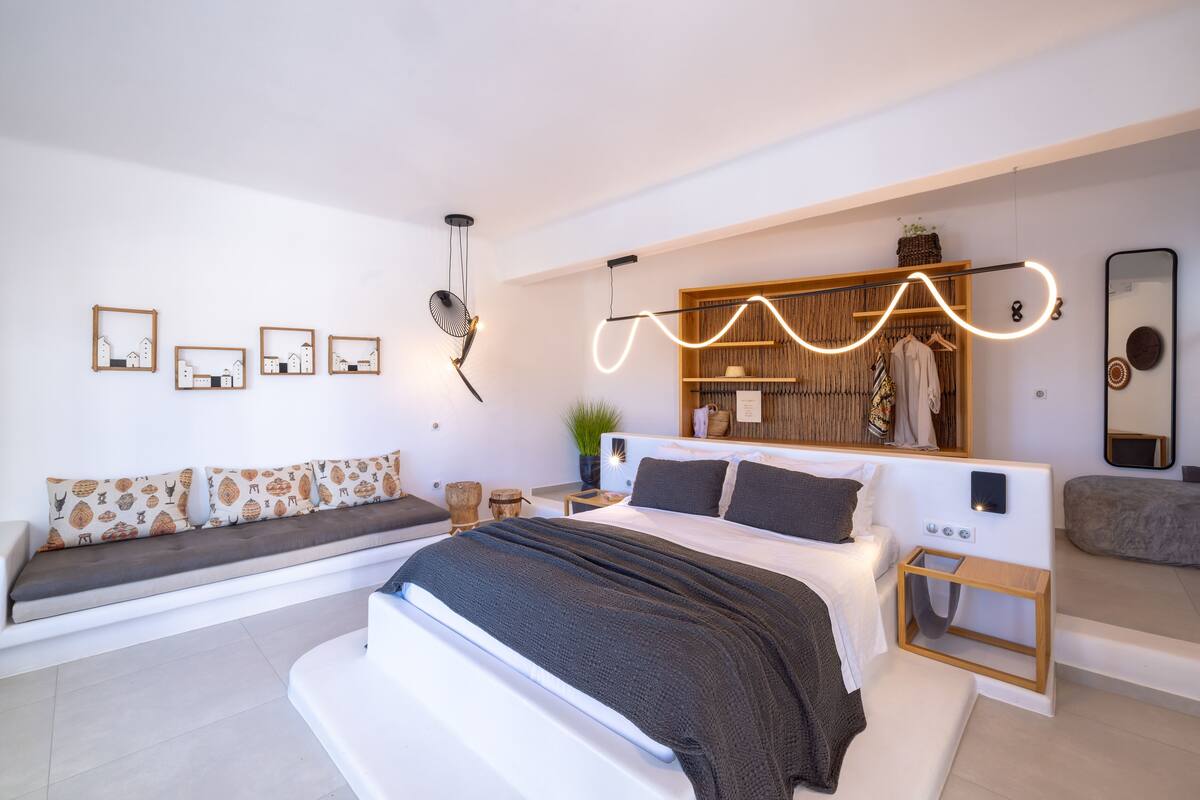 A modern bedroom with a large bed, bedside tables, a built-in wardrobe, and a seating area with cushions.