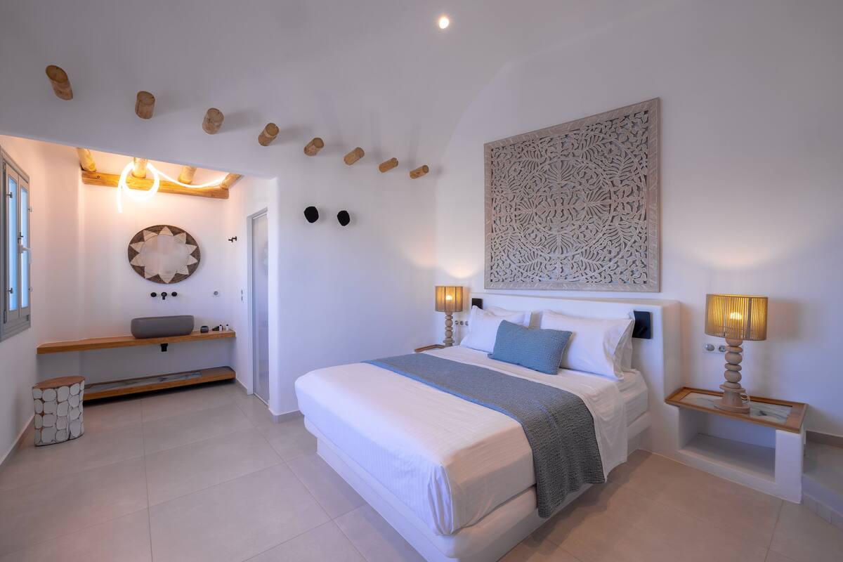 A modern bedroom with a large bed, bedside lamps, a decorative wall piece, and a built-in bench with storage.