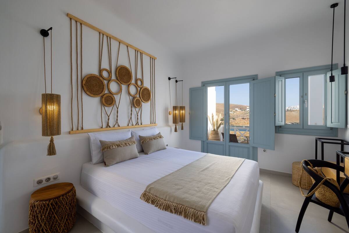 A bedroom with a bed, bedside tables, a hanging light fixture, and a window with a view.