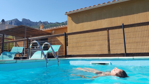 A swimming pool with a person swimming, lounge chairs, and a view of a mountain. - Air-conditioned vacation home with a pool: Gite Etape Cathare (Duilhac-sous-Peyrepertuse)