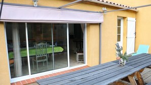 A patio with a wooden table and chairs, a sliding glass door leading to an indoor dining area, and a small potted plant on the table. - Air-conditioned vacation home with a pool: Gite Etape Cathare (Duilhac-sous-Peyrepertuse)