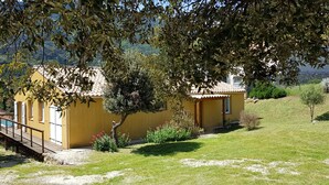 A yellow building with a tiled roof, a wooden deck, and a small garden with flowers. - Air-conditioned vacation home with a pool: Gite Etape Cathare (Duilhac-sous-Peyrepertuse)