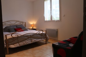 Une chambre à coucher avec un lit, une table de chevet, une lampe, un radiateur et une fenêtre.