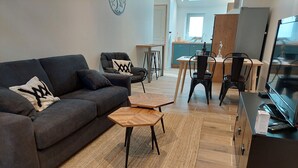 A modern living room with a sofa, two wooden side tables, a coffee table, and a kitchen area with a dining table and chairs. - Country house with jacuzzi (Cheilly-lès-Maranges)