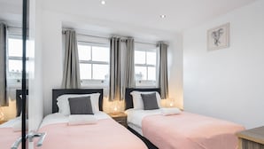 A hotel room with two beds, a wooden nightstand, a mirror, and a framed picture on the wall. - Cosy and Functional 1 Bedroom Flat in London (London)