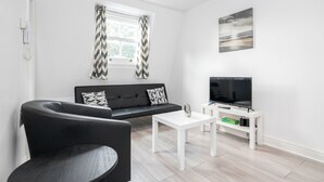 A modern living room with a black sofa, a white coffee table, and a TV on a white stand. - Cosy and Functional 1 Bedroom Flat in London (London)