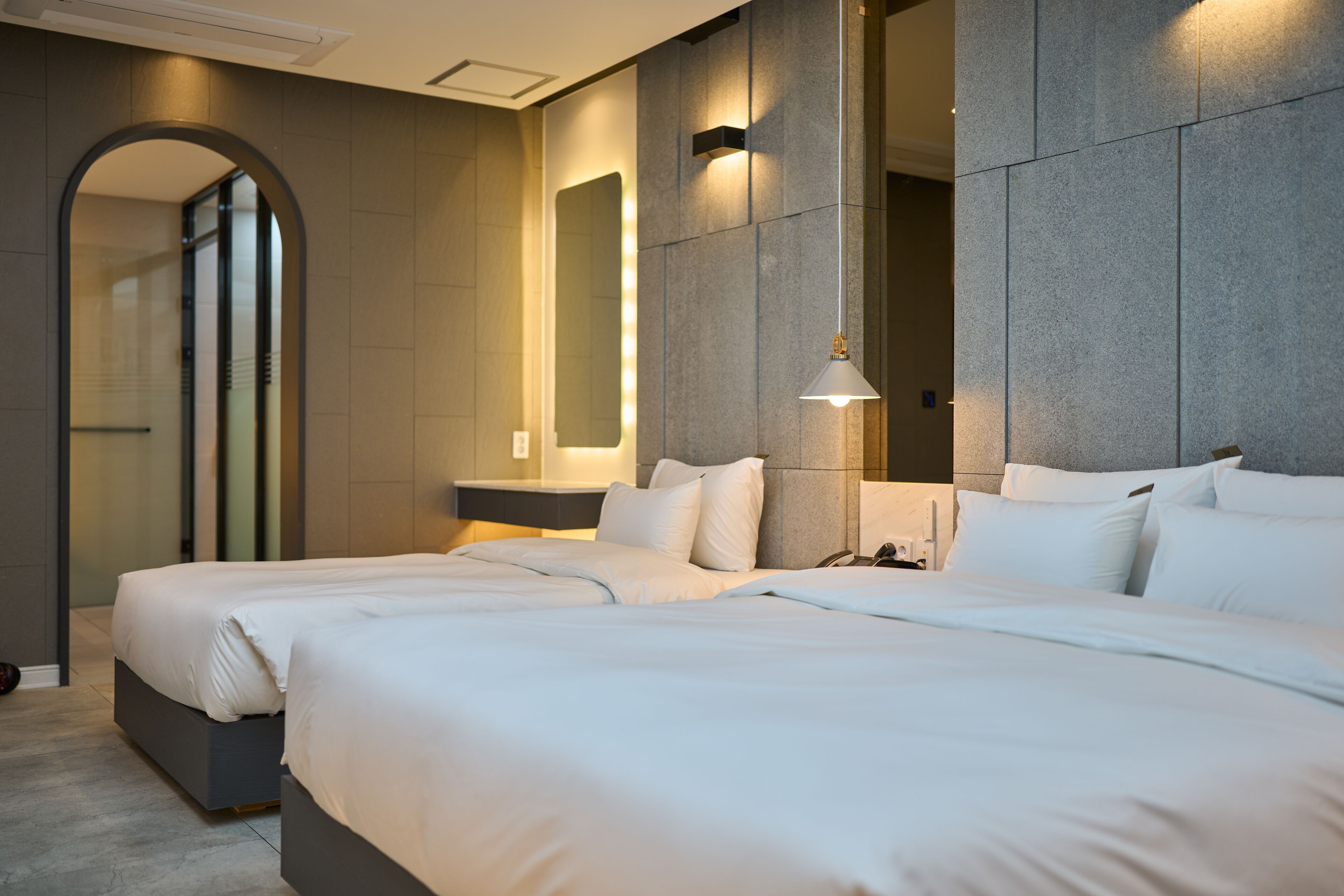 A modern hotel room with two beds, a large mirror, and a pendant light.