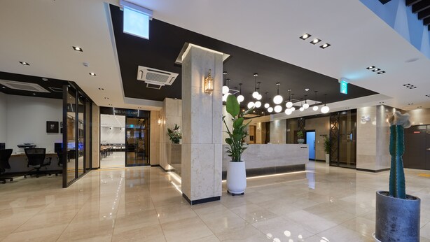 Um lobby moderno com balcão de recepção, uma grande planta em vaso e uma escadaria.