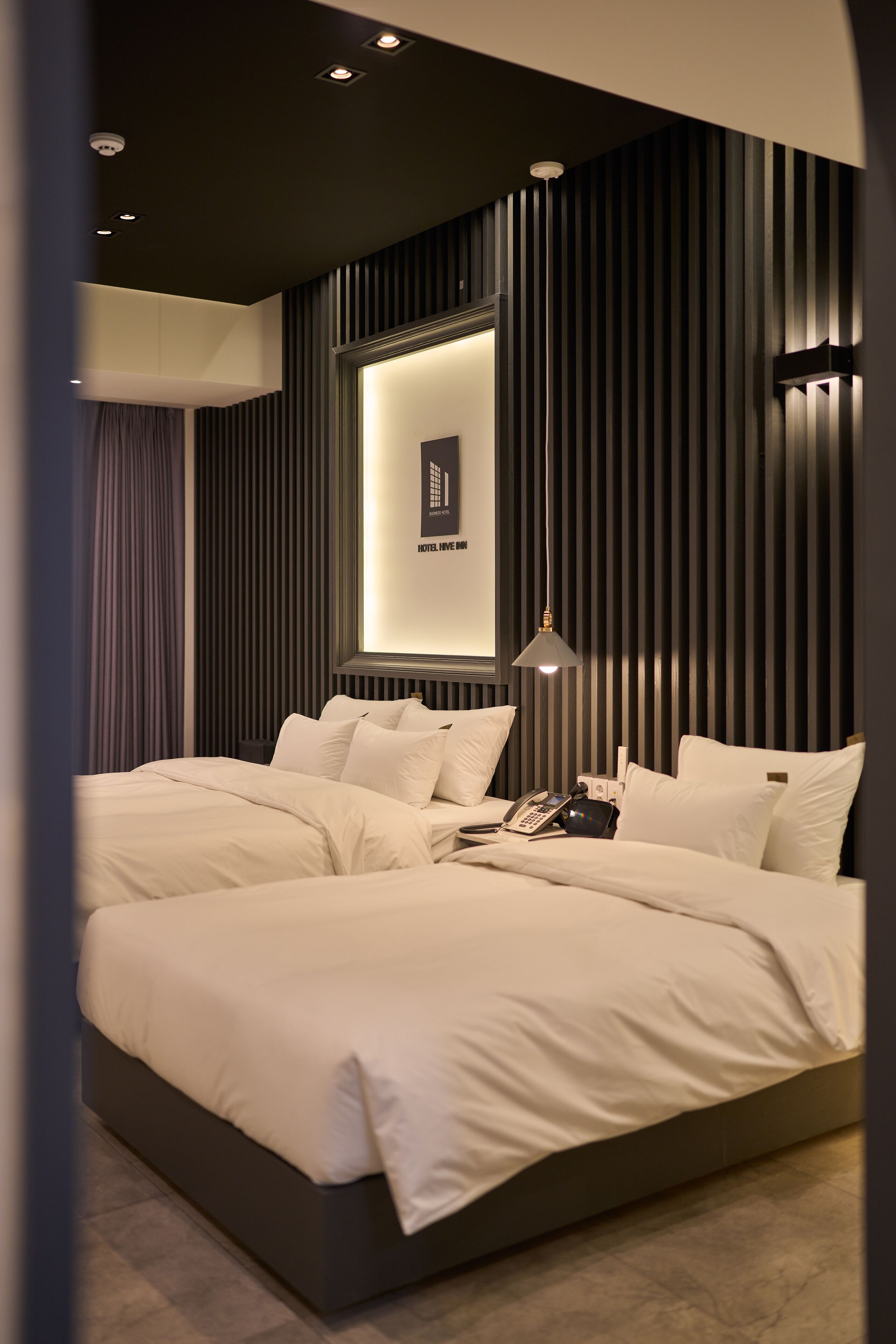 Une chambre d’hôtel moderne avec un grand lit, un téléphone sur la table de chevet et un luminaire fixé au mur.