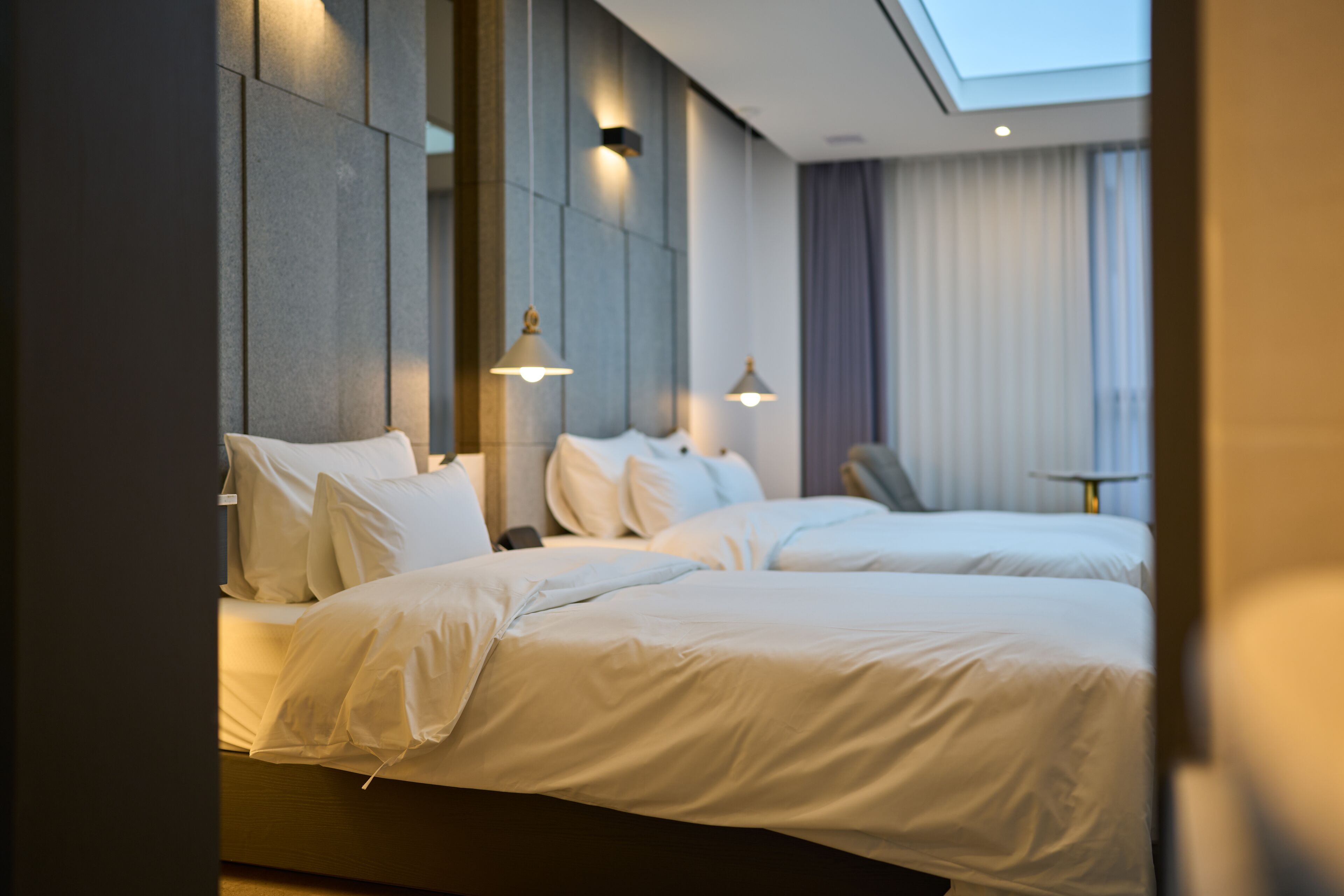 Una habitación de hotel moderna con dos camas, una mesita y vista al cielo a través de la ventana.
