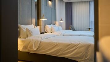 A modern hotel room with two beds, a small table, and a view of the sky through the window.