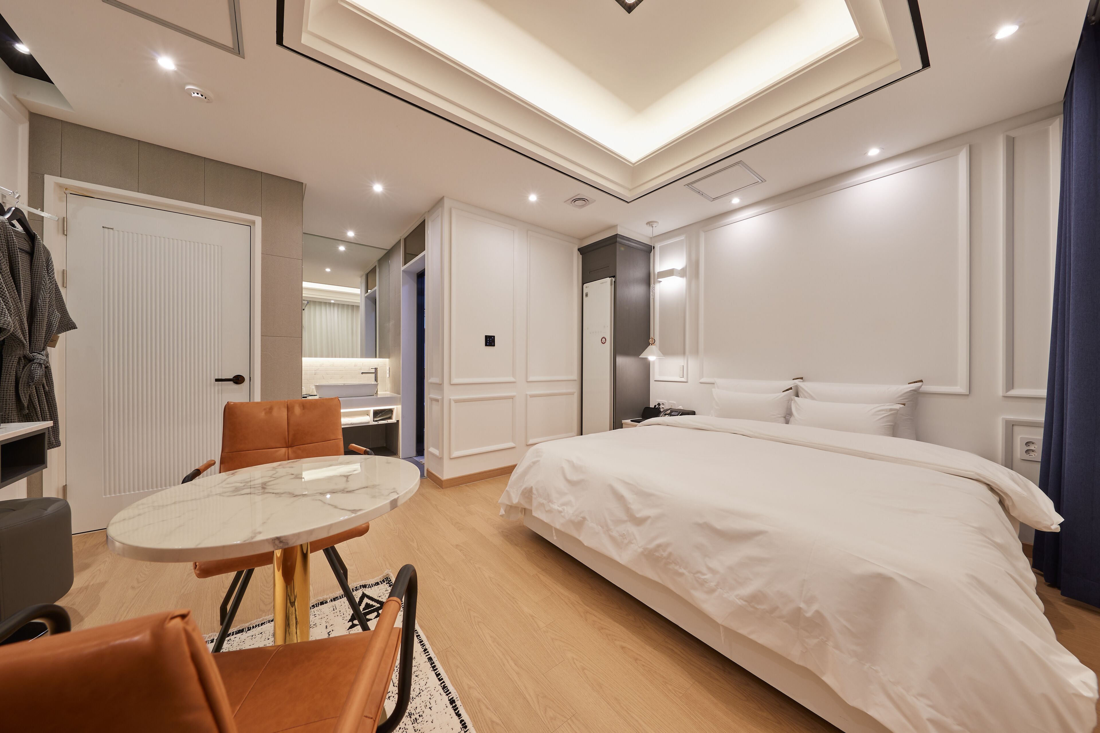 A modern hotel room with a large bed, a round dining table, and a seating area.