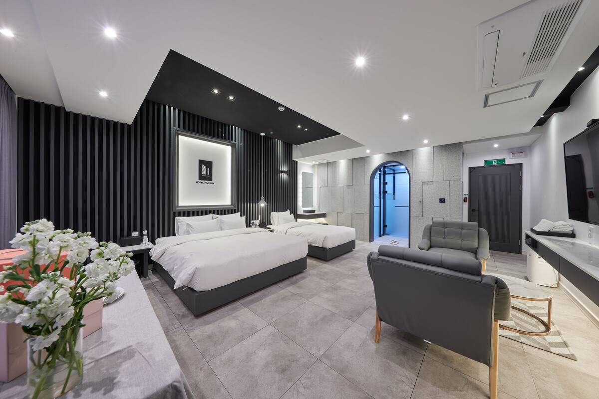 A modern hotel room with a large bed, a sofa, a desk, and a bathroom.