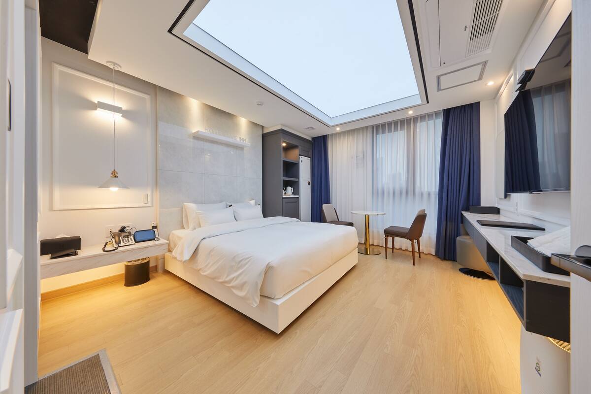 A modern hotel room with a large bed, a desk, and a skylight.