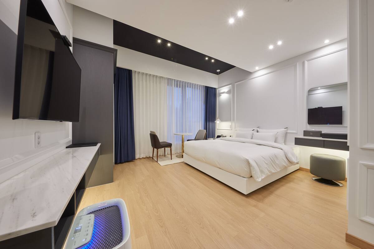 A modern hotel room with a bed, a desk, a chair, a TV, and a massage chair.