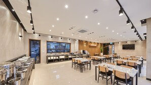 Uma sala de jantar moderna com várias mesas e cadeiras, um buffet com diversos pratos e um balcão de restaurante ao fundo.
