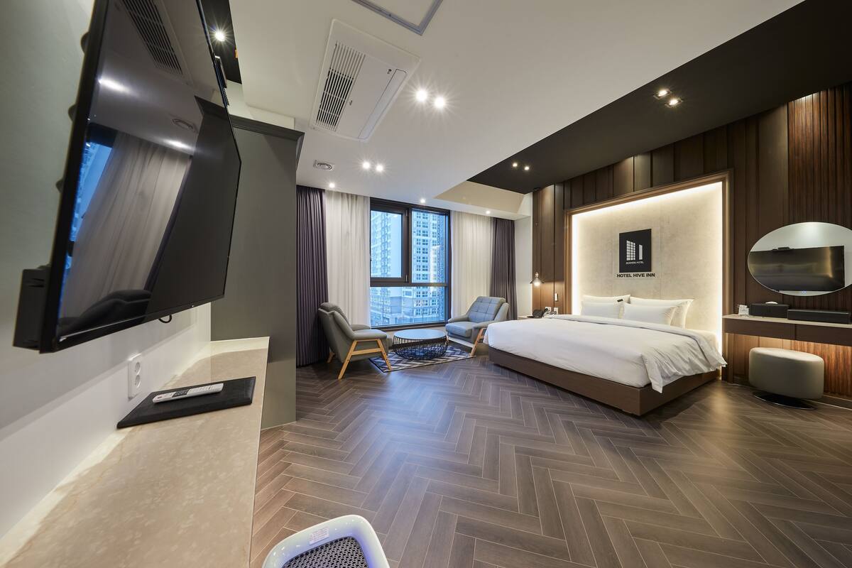 A modern hotel room with a large bed, a TV, a desk, and a view of the city.