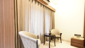 A room with a sofa, a chair, a small table, and a nightstand with a tray. - Hotel Kohinoor Plaza (Chhatrapati Sambhajinagar)