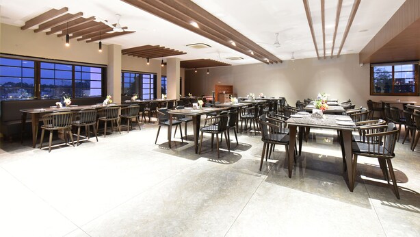 A spacious dining area with multiple tables and chairs, large windows offering views of the cityscape, and a modern ceiling design with recessed lighting. - Hotel Kohinoor Plaza (Chhatrapati Sambhajinagar)