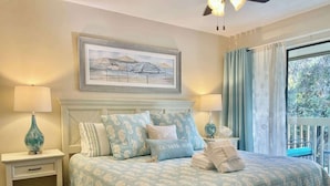 Une chambre à coucher avec un lit, deux tables de chevet, une commode, une fenêtre avec des rideaux et un tableau au mur.