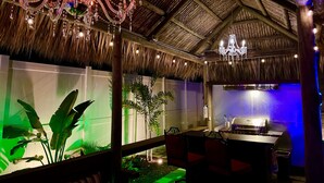 An indoor space with a thatched roof, a chandelier, and a dining area with a table and chairs.