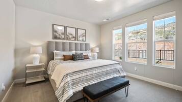 A bedroom with a bed, bedside tables, a bench, and large windows with a view of a desert landscape.