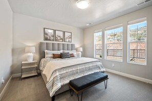 A bedroom with a bed, bedside tables, a bench, and large windows with a view of a desert landscape. - Lazy River Retreat by RedAwning (Washington)