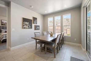 A dining area with a wooden table and chairs, framed artwork on the wall, and large windows offering a view of the outdoors. - Lazy River Retreat by RedAwning (Washington)