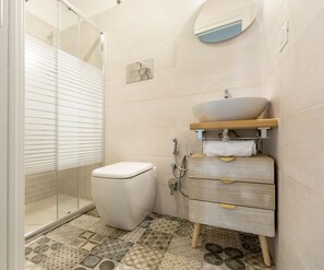 Een badkamer met toilet, een wastafel met spiegel erboven en een douche.