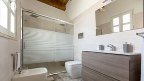 Een moderne badkamer met een douchecabine van glas, een wit toilet, een wastafel met spiegel en vloertegels met een patroon.