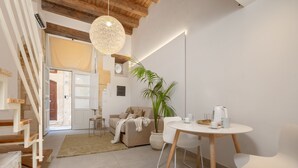 A modern living room with a staircase, a dining area with a table and chairs, a large potted plant, and a hanging light fixture. - Suite 2 Standard (Syracuse)