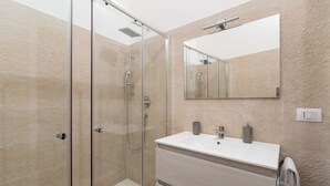 A modern bathroom with a glass-enclosed shower, a white sink with a mirror above it, and a towel rack. - Suite 4 Loft (Siracusa)