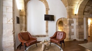 A stone-walled room with two leather chairs, a wooden coffee table, and a flat-screen TV mounted on the wall. - Suite 4 Loft (Siracusa)