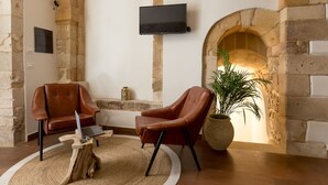 A cozy room with stone walls, a fireplace, two leather chairs, a wooden coffee table, and a flat-screen TV mounted on the wall. - Suite 4 Loft (Siracusa)