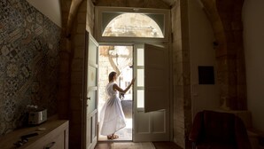 A woman in a white dress entering a room with a tiled wall and a stone archway. - Suite 4 Loft (Siracusa)