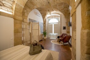 A hallway with stone arches, a wooden door, a chair, a table, and a hanging lamp. - Suite 4 Loft (Siracusa)