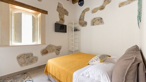 A bedroom with a bed, a window, a TV, and stone wall decorations. - Suite 5 Superior (Siracusa)