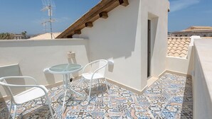 Una terraza en la azotea con suelo de baldosas, una pequeña mesa redonda, dos sillas blancas y una estructura de vigas de madera.