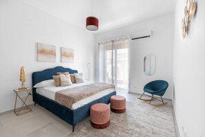Un dormitorio con una cama grande, dos otomanes, un sillón mecedor e iluminación colgante.