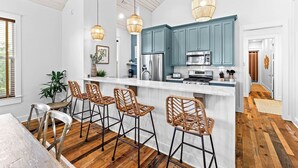 Una cocina moderna con una isla central, taburetes de bar y un comedor con mesa de madera.