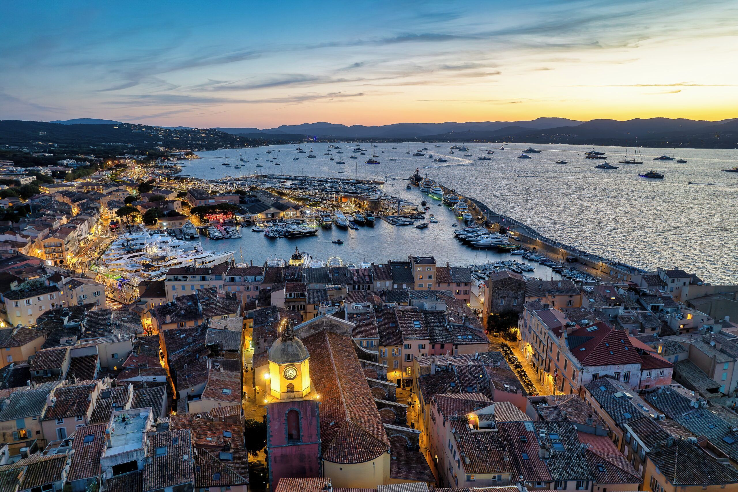 A coastal town with historic buildings, a prominent clock tower, and a marina with boats.