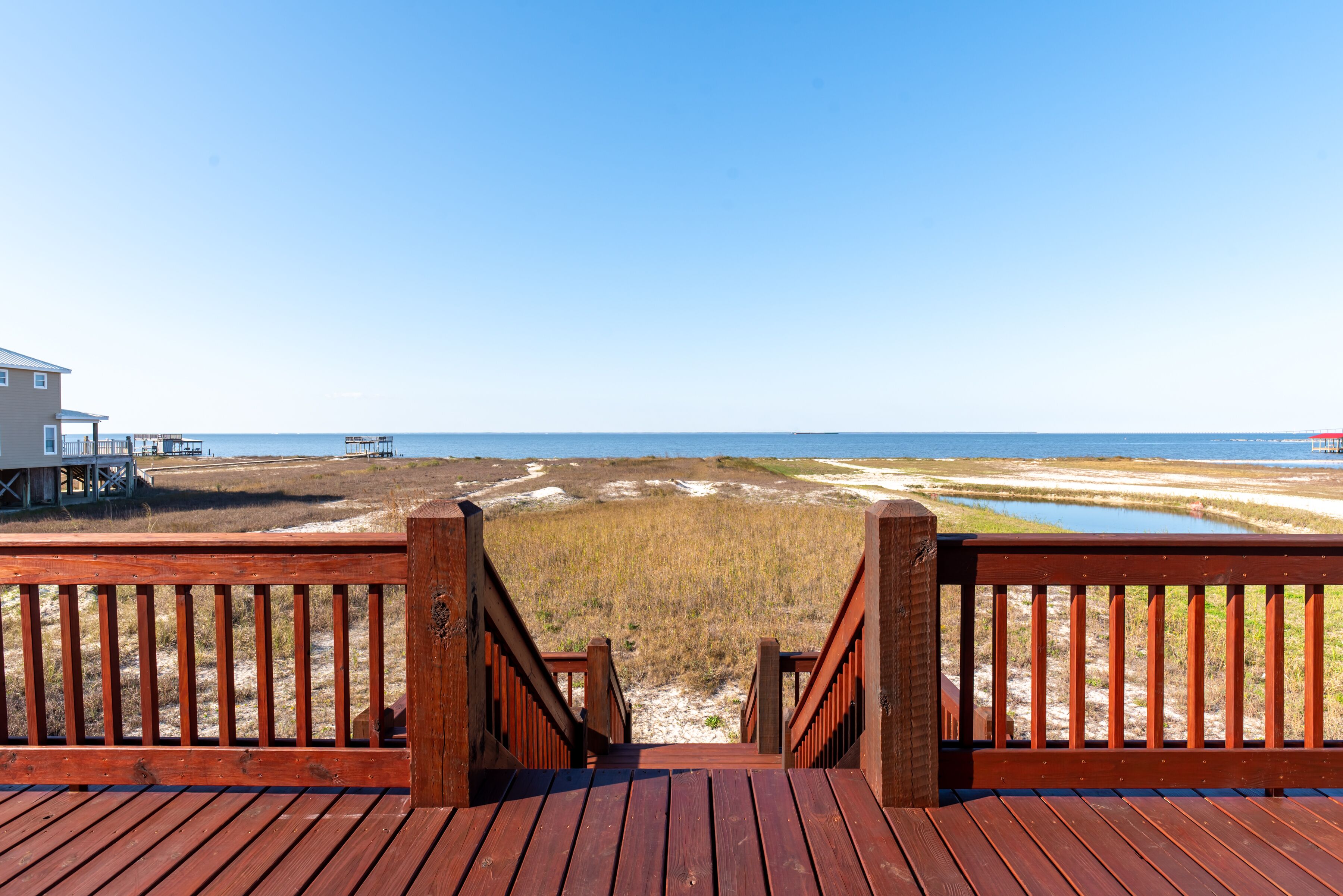 A wooden deck leading to a beach with a clear view of the ocean and dunes.