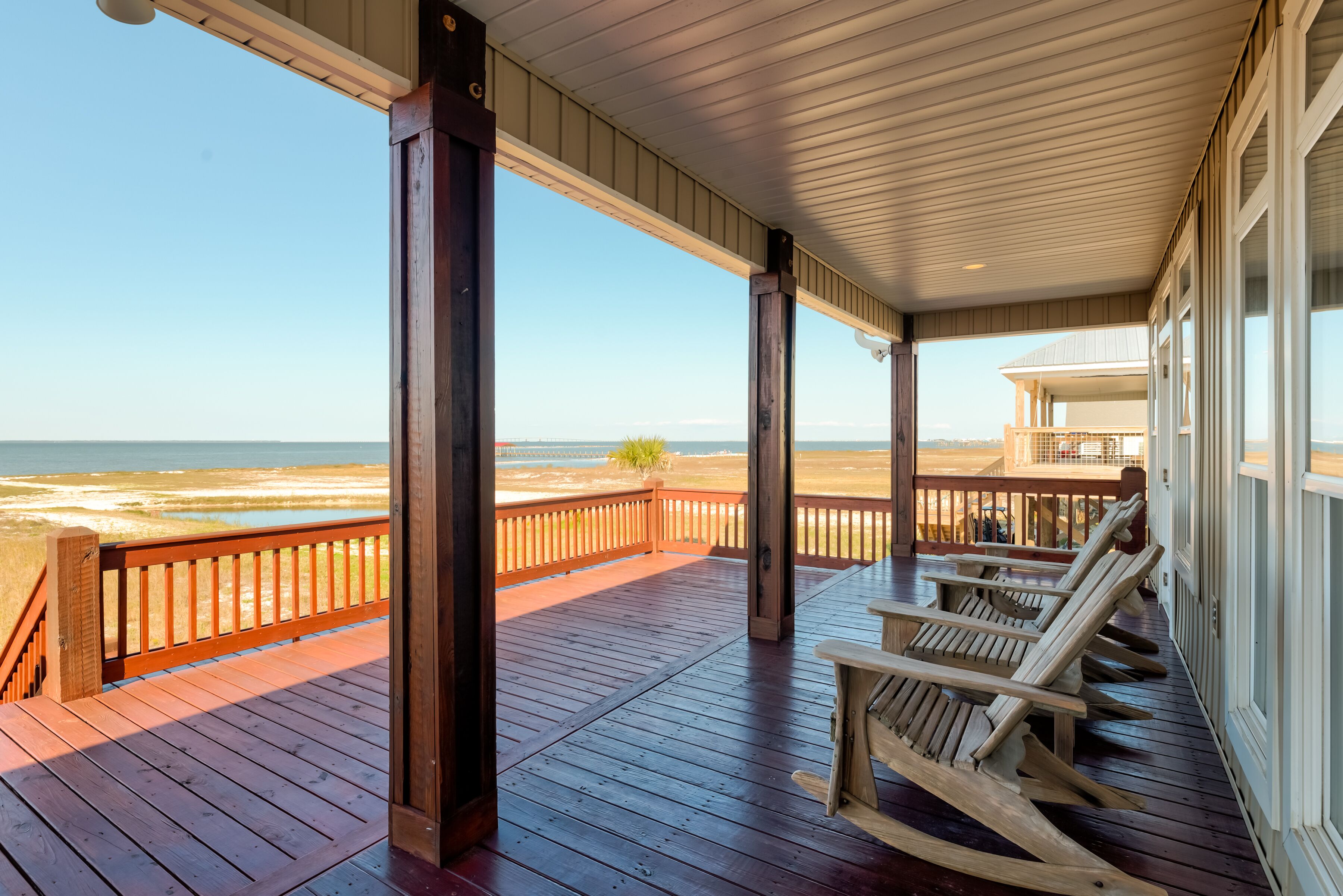 A wooden deck with a view of the beach, wooden chairs, and a covered area with a railing.