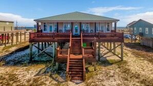 Une maison de plage dotée d’un porche abrité, d’un escalier menant à l’entrée principale et offrant une vue sur l’océan.