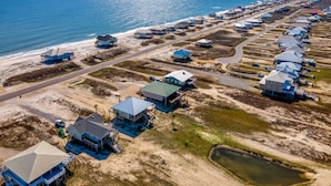 Vue aérienne d’un complexe côtier comprenant plusieurs maisons sur pilotis, une plage et une vue dégagée sur l’océan.